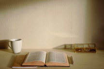 open Bible, coffee mug, journal, pen, and basket on a desk 