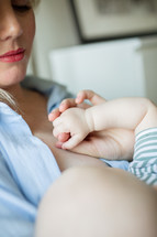 Infant holding mom's hand while nursing 