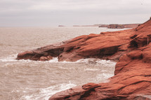 waves washing over red rocks along a shore 