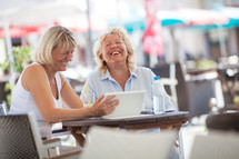 Senior women laughing while using tablet PC in cafe