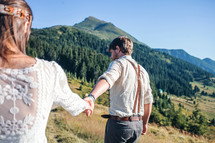 bride and groom holding hands walking through a mountain landscape 