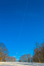 plane contrail in a blue sky over snow covered ground 