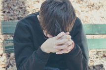  a teen boy with head bowed praying 