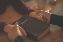 a couple holding hands in prayer near a Bible 