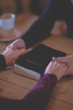 a couple holding hands praying near a Bible 