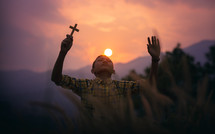 a boy holding a cross praying at sunset 