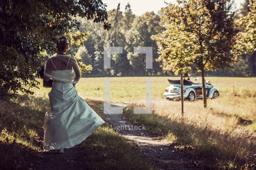 bride walking down a dirt road towards a convertible 