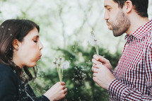 man and woman blowing dandelions 