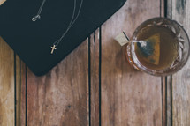 cross necklace on a Bible and glass of tea 