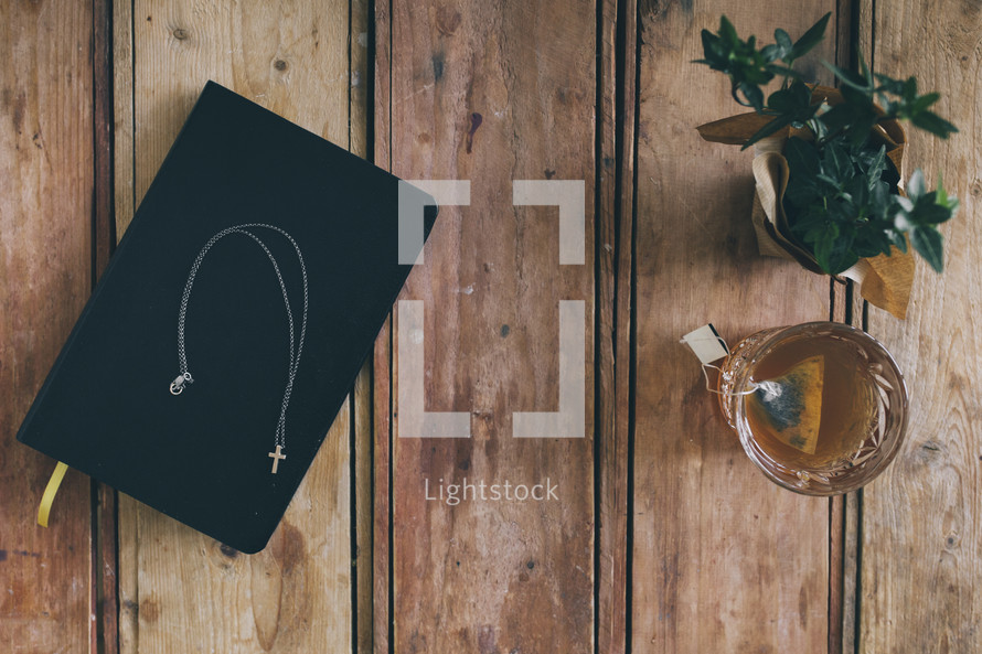 cross necklace on a Bible, houseplant, and glass of tea 