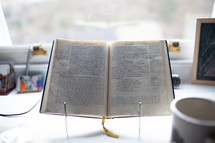 open Bible on a stand in a window on a desk 