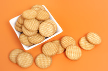 A white plate full of round crackers on an orange surface.
