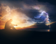 silhouette of a man praying during a storm 
