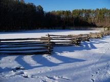 A wooden fence cascades across the landscape covered by fresh snow on a winter day in Virginia.