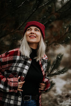 Portrait of young pretty woman in forest, winter season. Attractive kind blonde girl smiling, lady in knitted hat. High quality