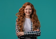 Pretty red long curly haired woman in hipster plaid shirt, natural beauty. Young girl on blue, charming eyes. American white appearance looking at camera. High quality 