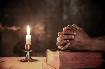 a man praying over a Bible in candlelight 