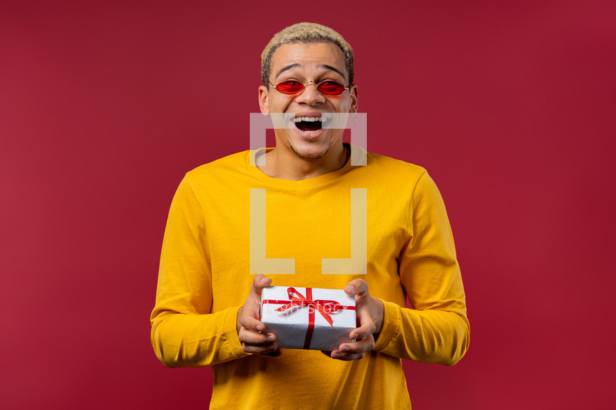 Stylish man with gift box on red background