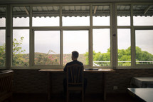 a man sitting at a table looking out a window in thought 