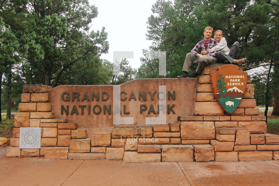couple sitting on the Grand Canyon National Park sign 