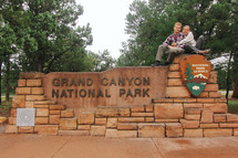 couple sitting on the Grand Canyon National Park sign 