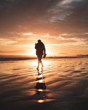 silhouette of a person walking on a beach at sunset 