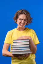 Lazy woman student is dissatisfied with amount of books homework on blue background. Girl with short hair in displeasure, she is annoyed, discouraged frustrated by studies. High quality photo