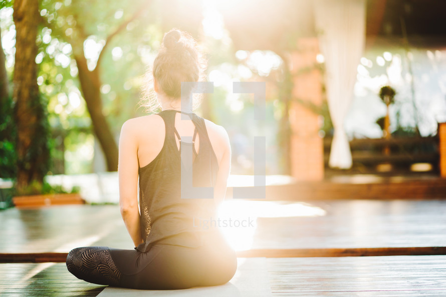 Young woman practicing yoga alone on wooden deck in tropical island. Sport, fitness, healthy lifestyle concept