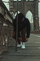 a man tying his shoes on a bridge 