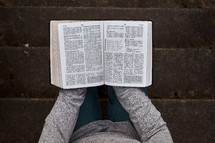 a young man sitting on steps reading a Bible 