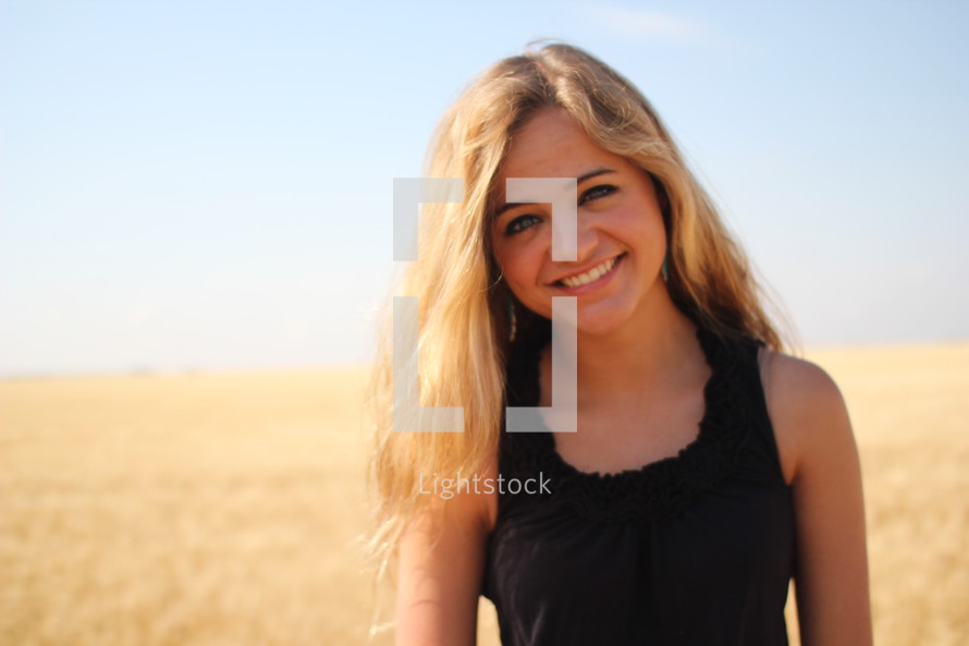 a smiling young woman standing in a field of brown grains 