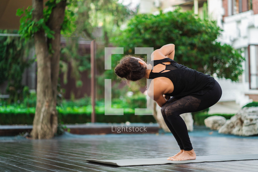Young woman practicing yoga alone on wooden deck in tropical island. Sport, fitness, healthy lifestyle concept