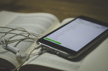 Bible app on a cellphone and earbuds on an open Bible 