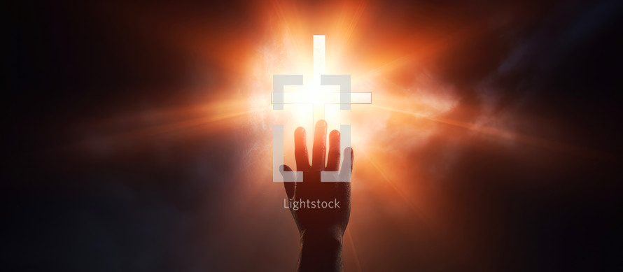 Hand reaching for the cross with light rays on a dark background 