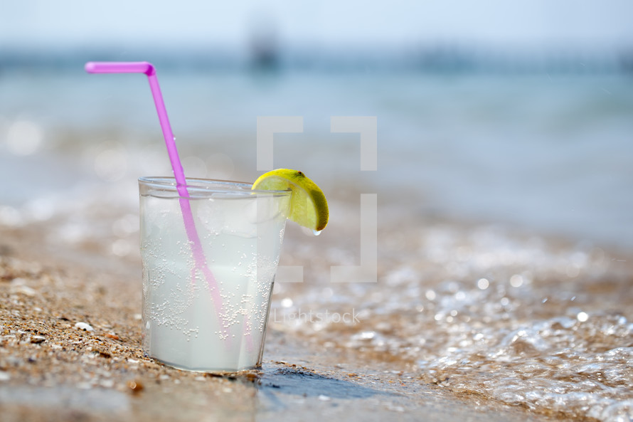 Glass of lemonade or water on beach by sea