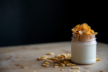 jar of yogurt with cornflakes stands on a wooden board and black background