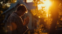 Man praying in front of his house in the sunset light.