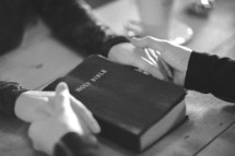 Two people holding hands around a Bible - black and white
