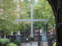 Christian cross on a church window glass, blurred trees in the background