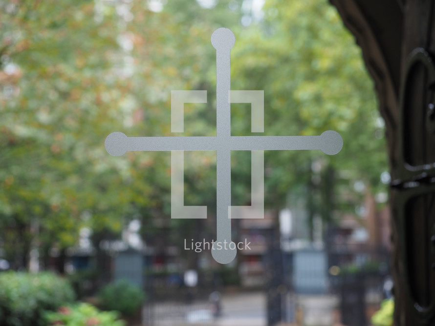 Christian cross on a church window glass, blurred trees in the background
