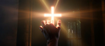 Hands touching a glowing cross in the dark 