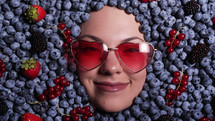 Smiling woman face in fresh ripe blueberries. Young attractive girl covered with acai berries. Lady with bright makeup. enjoying organic bilberry plant. Diet, antioxidant, healthy vegan food.