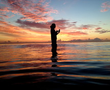 silhouette of a woman standing in water at sunset 