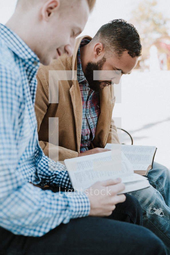 two men reading a Bible and discussing scripture while sitting on a park bench 