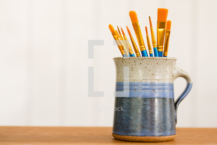 a blue mug of paint brushes with a white background