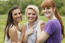 three young women, standing together hugging, outside in a field