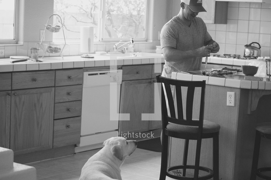 a man cooking in the kitchen and a watchful dog 