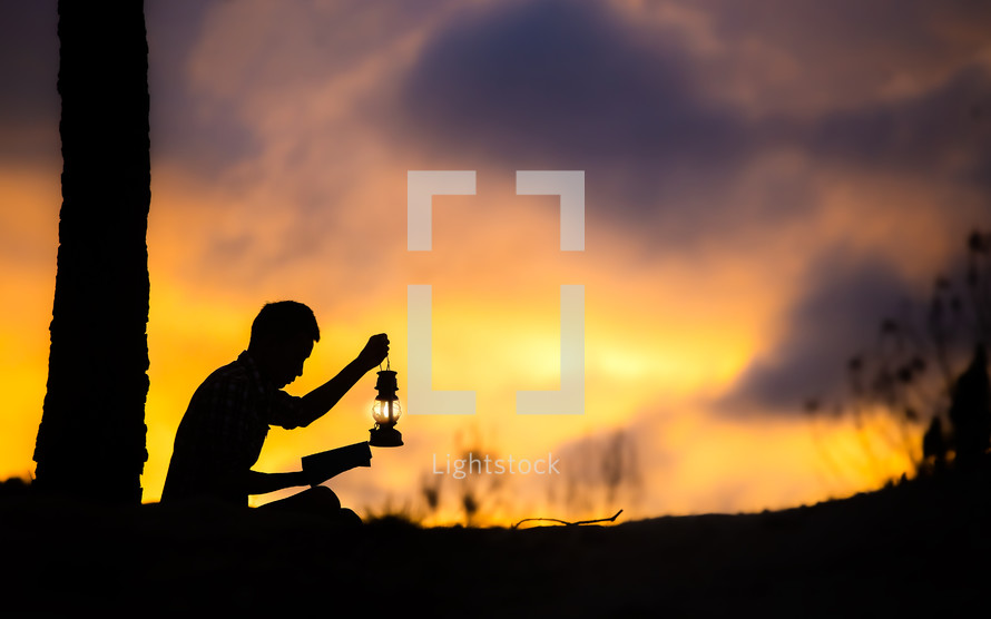 silhouette of a boy praying outdoors at sunset holding an oil lamp 