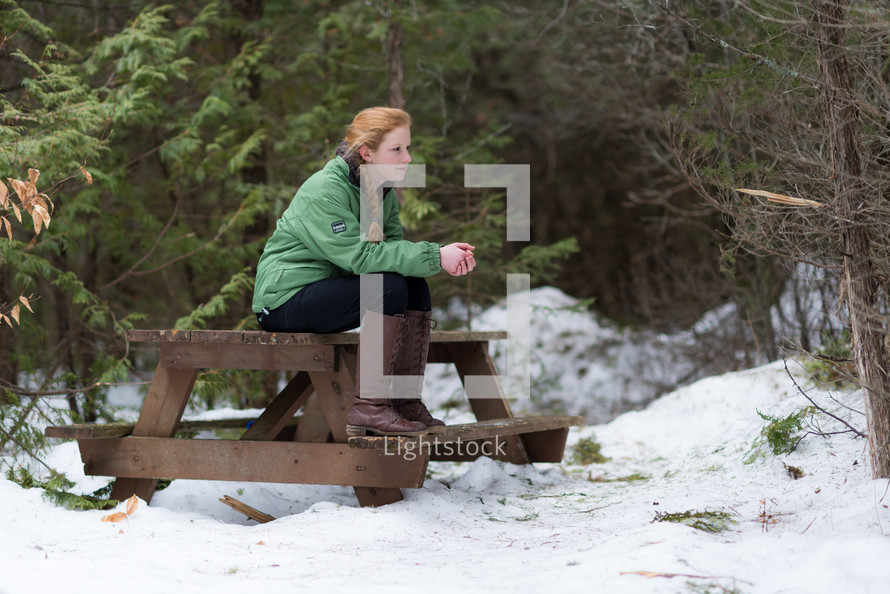 a teen girl sitting on a picnic table outdoors in snow 