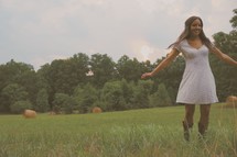 a young woman in cowboy boots dancing in a field with hay bales 